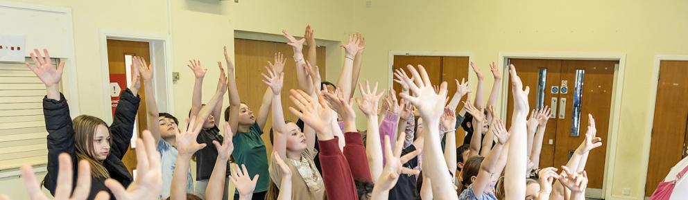 A room full of children with their hands in the air.