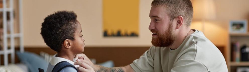 Man bending down straightening a small boy's school uniform collar