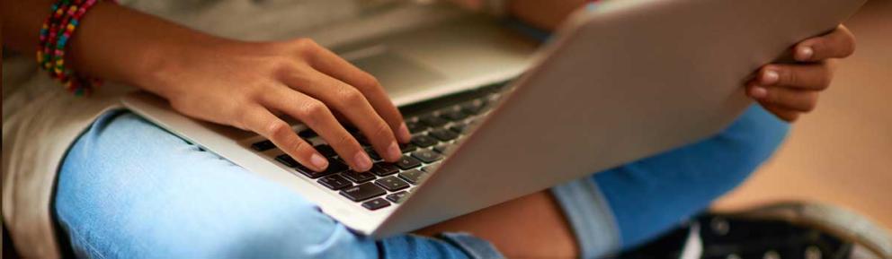 Young person sitting cross legged on the floor with a laptop.