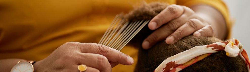 A close up of a black woman combing out a black child's hair using an afro comb.