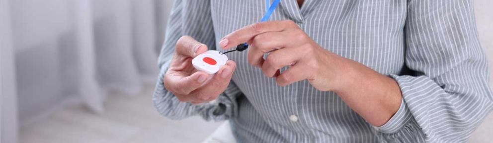 Torso of person wearing striped shirt with care alarm in one hand