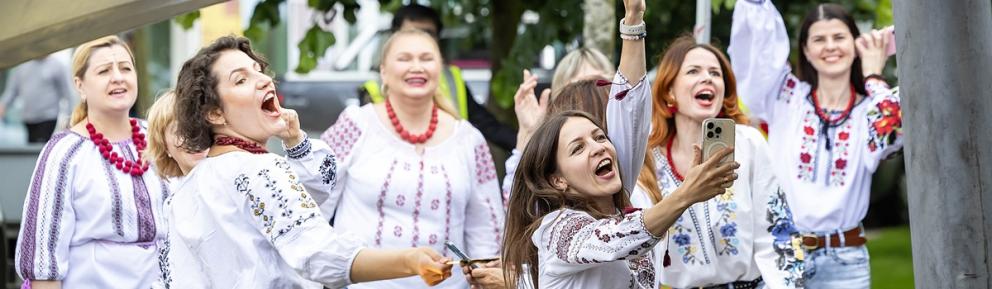 A group of women wearing jeans and traditional embroidered tops laugh and pose for a selfie.