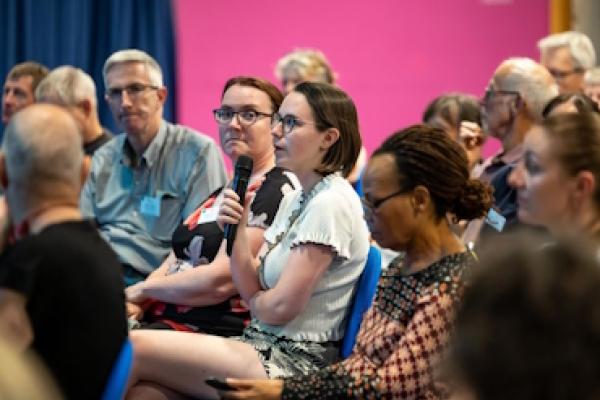 A woman holds a microphone and asks a question towards the stage.