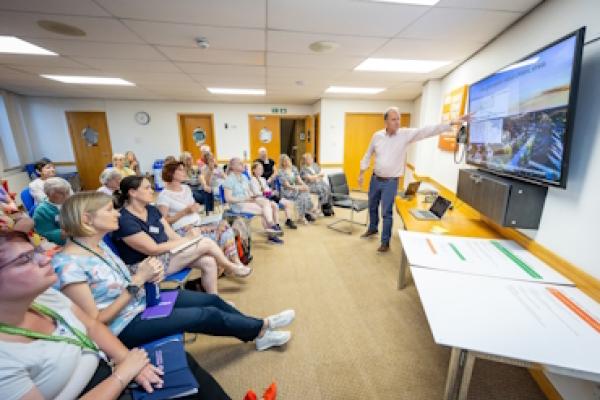A man stands in front of a seated crowd and points at a screen during a workshop at the Bracknell Forest climate summit.