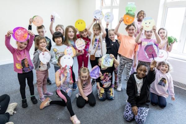A big group of children show off paper plates which they've designed and decorated.