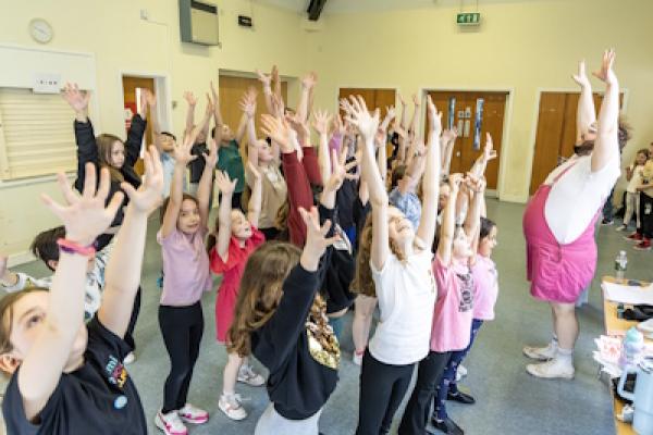 A group of children dance with their hands raised in the air.