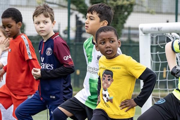 A row of keen-looking children wearing football kits stand on a pitch waiting for instructions. 