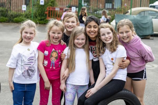 A group of 7 girls on a playground smile widely at the camera.