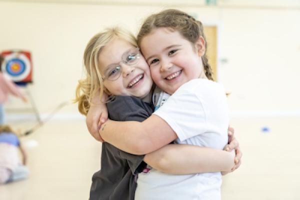 Two small children share a big hug with enormous smiles on their faces.