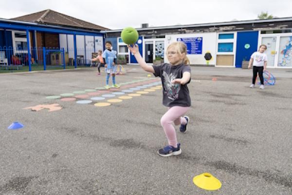 A young girl throws a green foam ball with a determined look on her face.