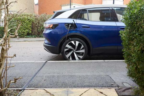 Blue electric vehicle parked on the street being charged by a cable in a cross-pavement charging gully.