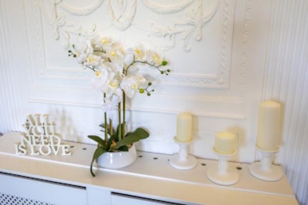 Decorations in the Haversham Room. There is a wooden cutout which says "All you need is love," a white potted plant and three tall candles.