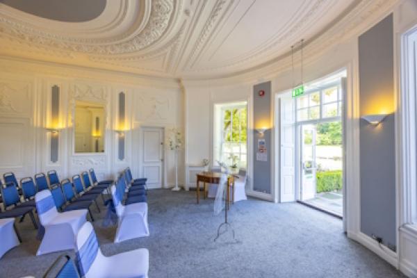 The Haversham Room from the side, with rows of chairs facing the wide double doors showing the gardens beyond.
