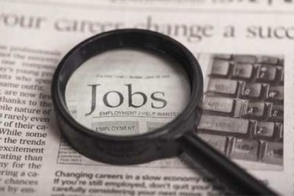 Magnifying glass laying on a newspaper over the word jobs.