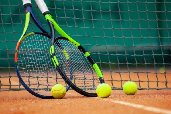 Two tennis racquets and 3 balls on a court by the net