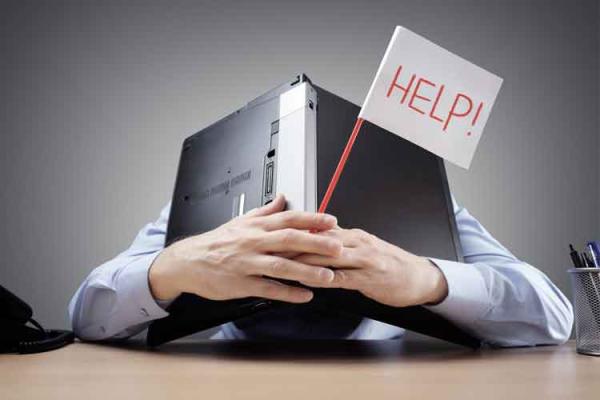 Person crouched over a desk with an upside down laptop and a flag that says "Help!"
