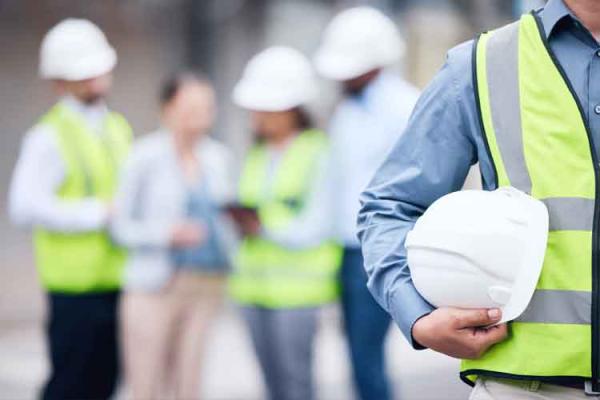 Person with yellow high vis vest on holding a white hard hat