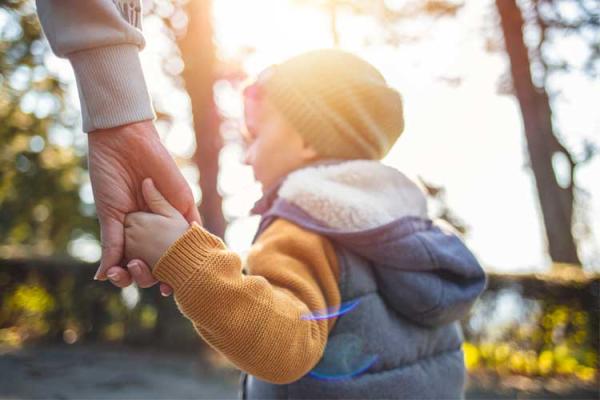Child holding hands with an adult in a park