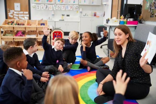 a teacher and pupils sitting on the floor in a classroom