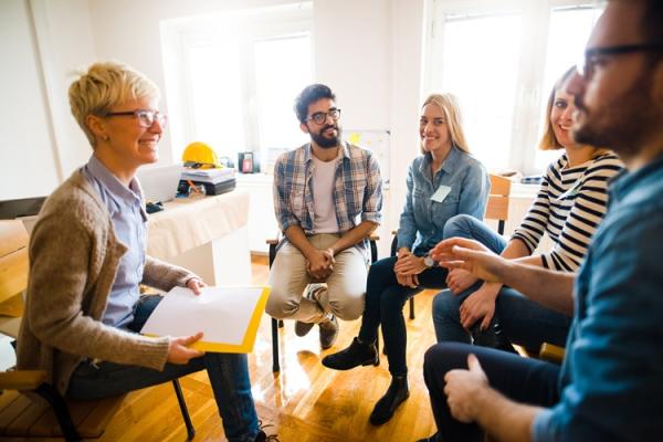 A small group of adults sits in a circle in a bright room, talking together.