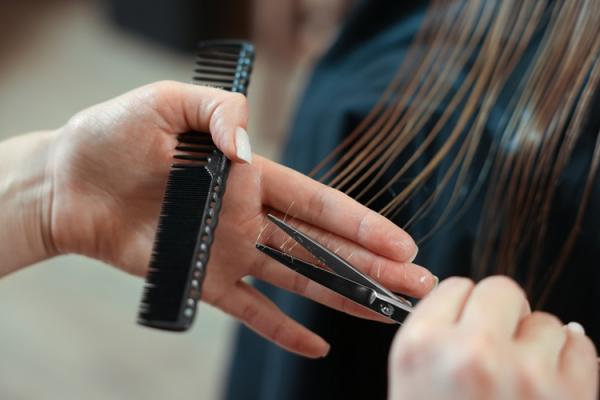 Close up of a hairdressers hand holding scissors and a comb and cutting long hair