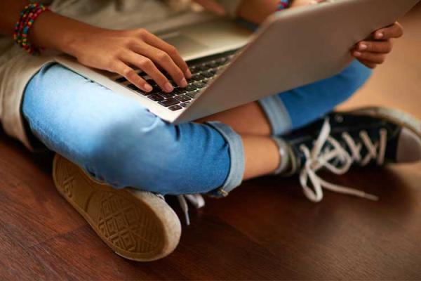 Young person sitting cross legged on the floor with a laptop.