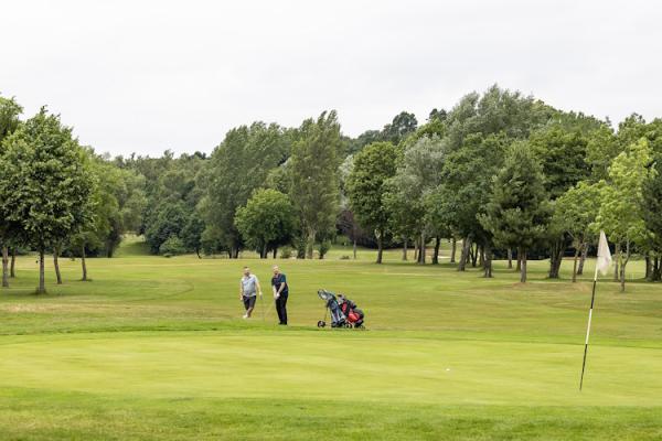 Two men play golf on a wide green.