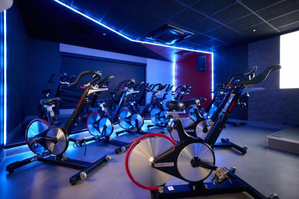 A row of stationary bikes in a gym, lit from behind with white lights.