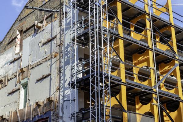 A building in the process of being demolished. There is exposed plaster on one side and heavy-duty scaffolding on the other.