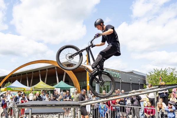 A man on a stunt bike does a wheely down a thin ramp in front of a crowd of people.
