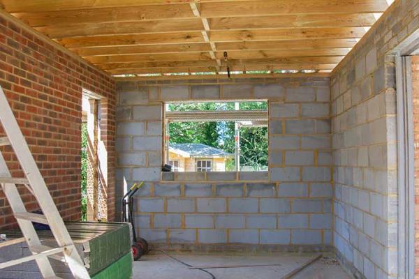 A residential extension with unpainted brick walls and slatted wooden roof with ladder in the corner