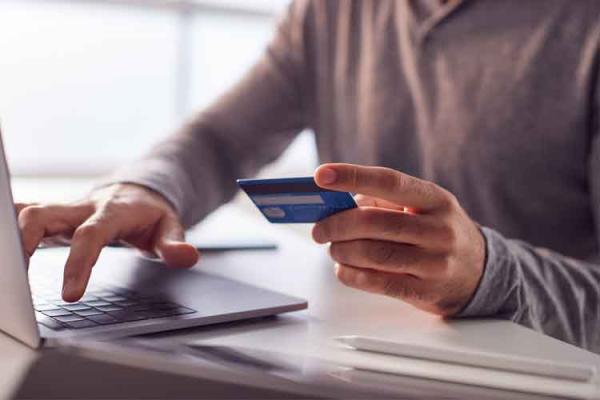 Person typing on laptop holding credit card