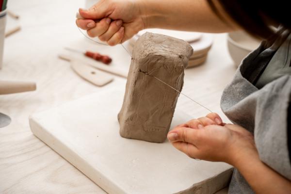 A person cuts through a lump of air-drying clay with a wire.