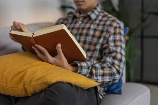 Man in checkered shirt, lounging on a couch with a book on his lap