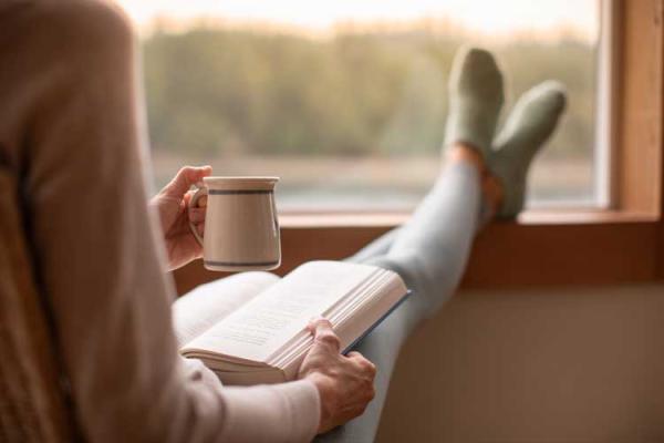 Person sitting down a book and a hot drink, by a window