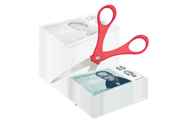 Red-handled scissors cutting through a stack of British banknotes.